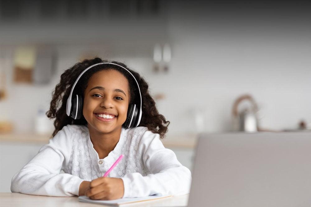 Ohio Connections Academy student in a white sweater looking at the camera smiling while taking an online class. 