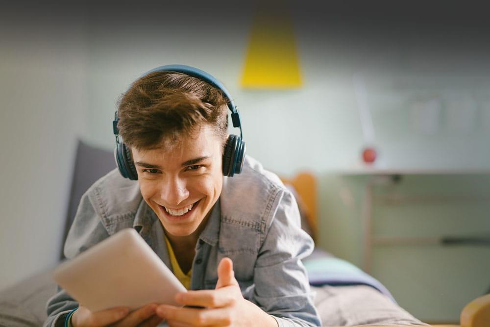 Young teen boy wearing headphones and looking at a tablet takign an online class for Wisconsin Connections Academy
